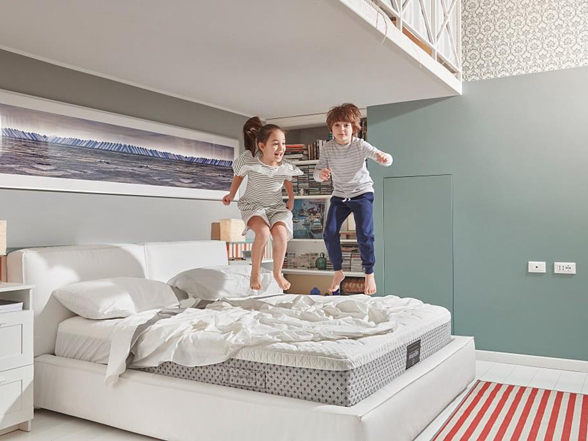 Skaczące dzieci na materacu w rodzinnym pokoju z dużym oknem Skaczące dzieci na materacu w rodzinnym pokoju z dużym oknem