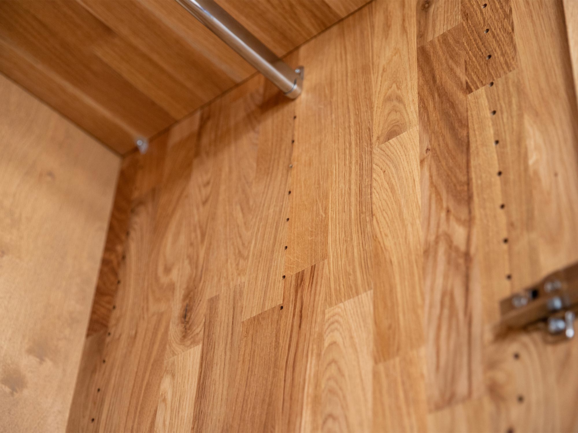 Zbliżenie na wnętrze szafy z drewna dębowego i chromowanym drążkiem