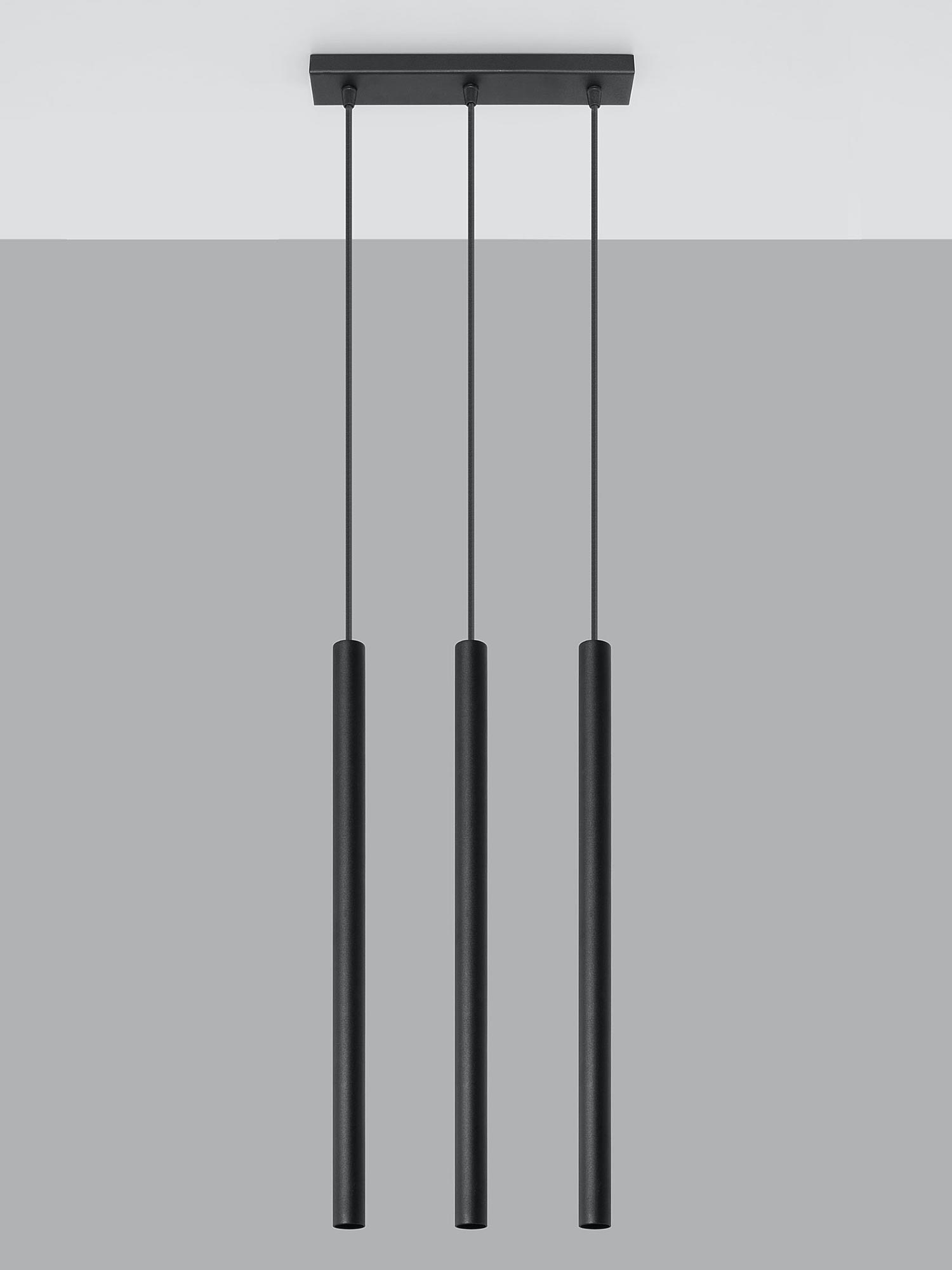 Trzy wiszące lampy pionowe w nowoczesnym wnętrzu z ciemną ścianą Trzy wiszące lampy pionowe w nowoczesnym wnętrzu z ciemną ścianą