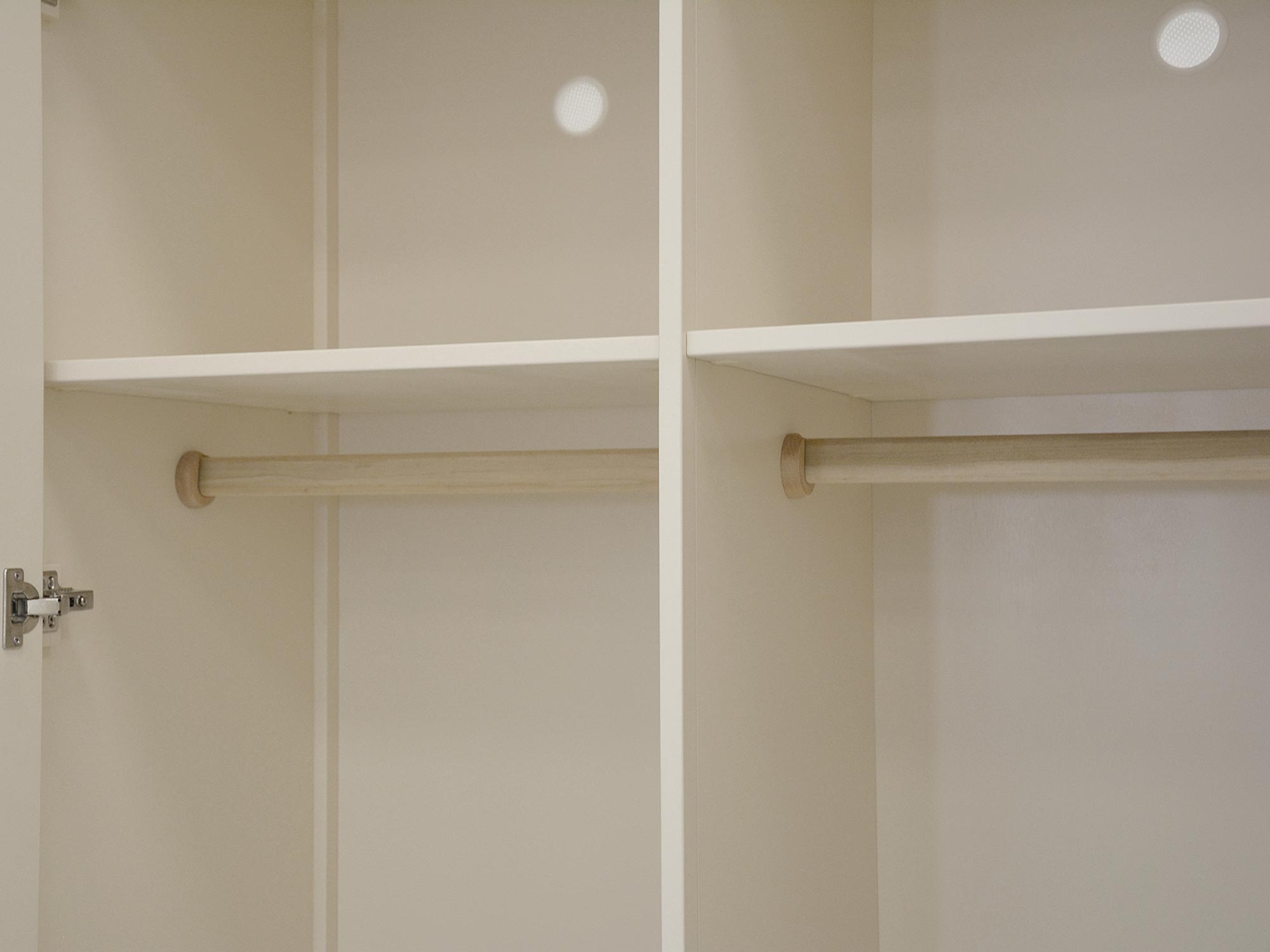 Wnętrze szafy drewnianej z drążkami na ubrania w kolorze ecru