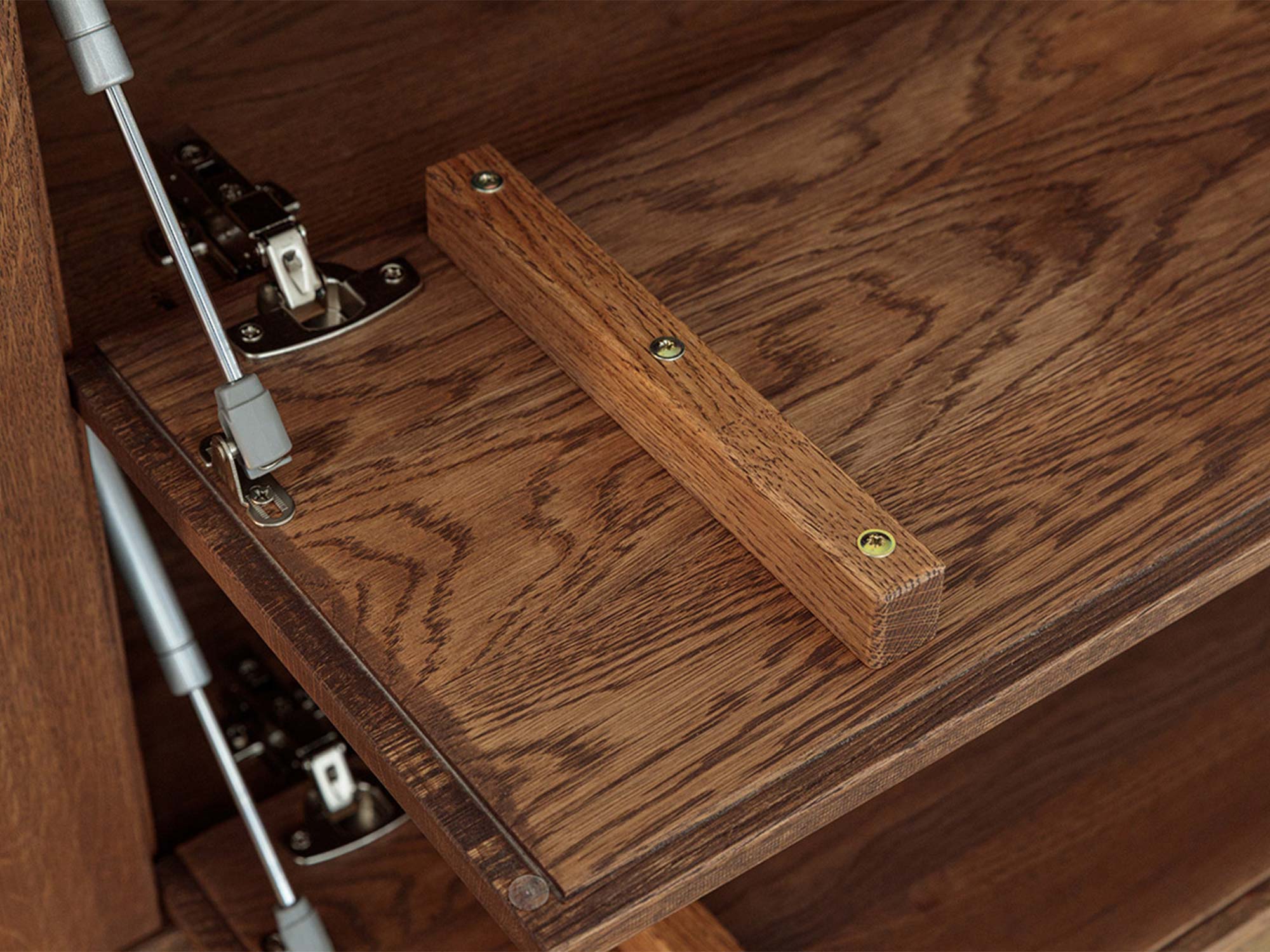 Detal klapy komody tabacco z siłownikami i drewnianym uchwytem