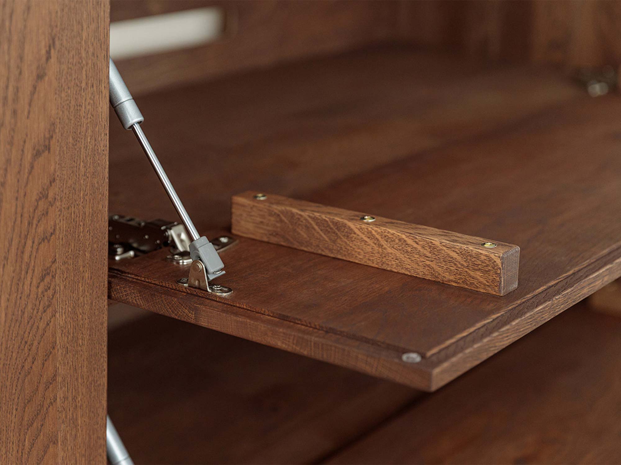 Detal otwartej klapy komody tabacco z siłownikiem gazowym zbliżenie