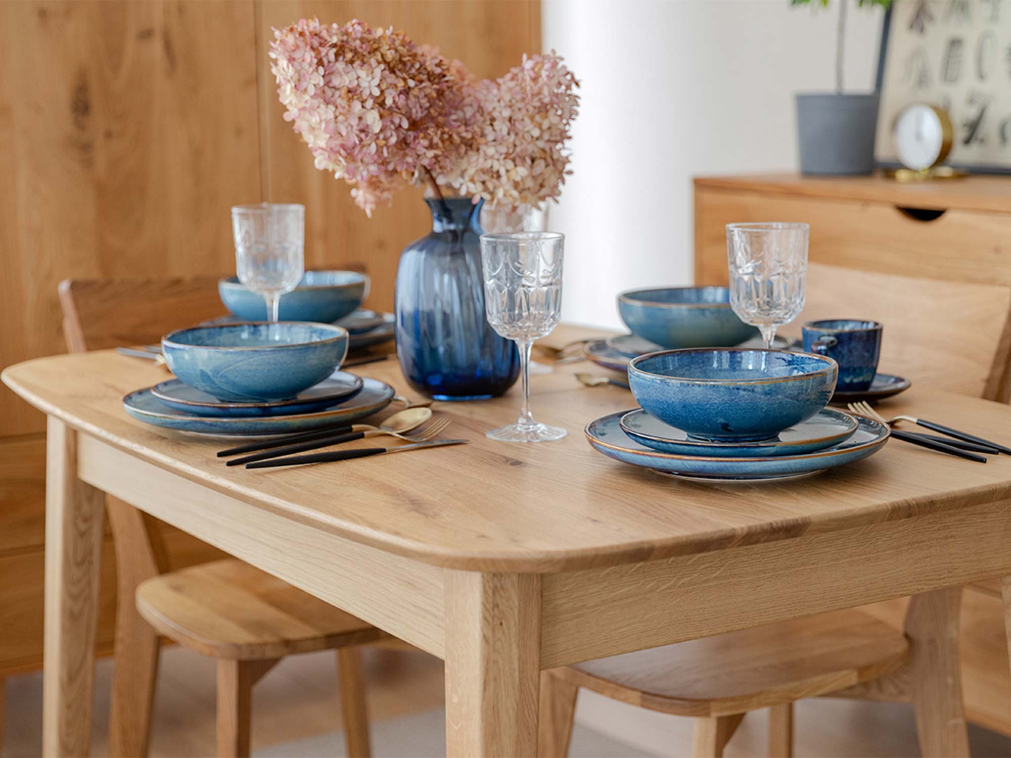 Dębowy stół jasny w aranżacji jadalni z niebieską ceramiką i kwiatami