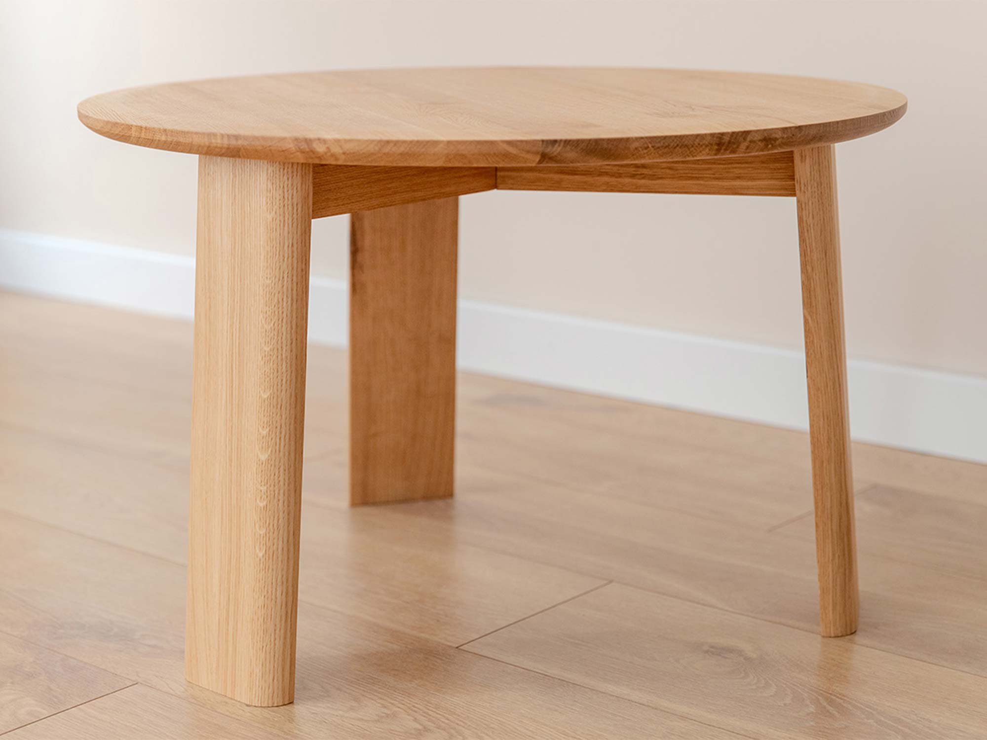 Stolik kawowy okrągły dębowy z trzema nogami na drewnianej podłodze