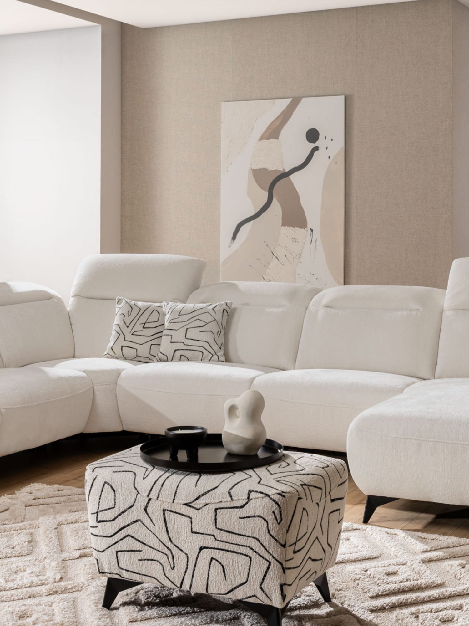 Polsterhocker Nelvaro vor dem Ecksofa im Wohnzimmer